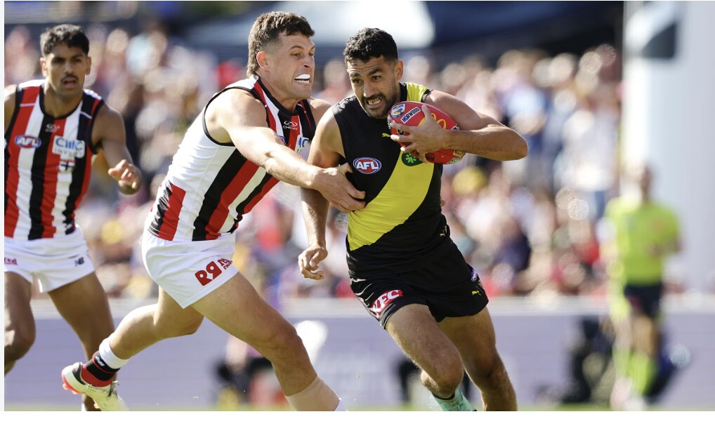 An AFL player breaking a tackle and running with the ball during an Australian rules football match in a packed stadium