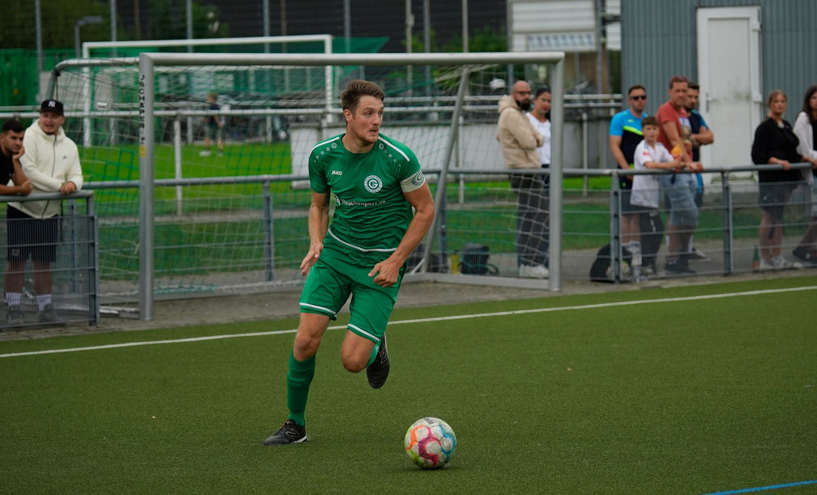 A footballer driving forward with the ball during a European club match watched by local supporters