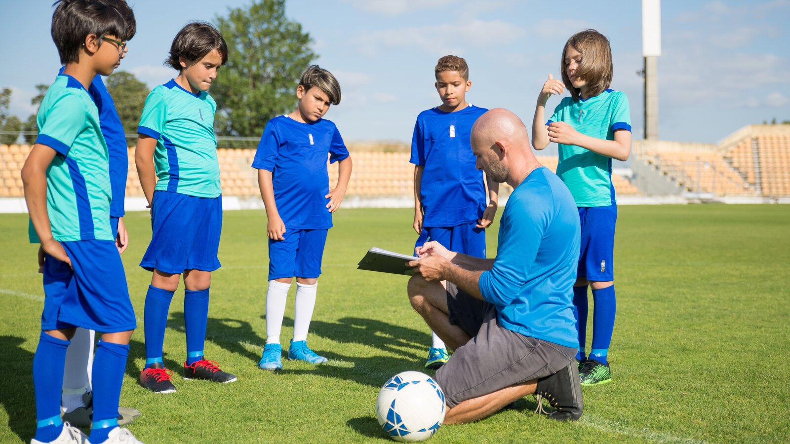 A coach instructing a youth football team on a pitch in an educational setting