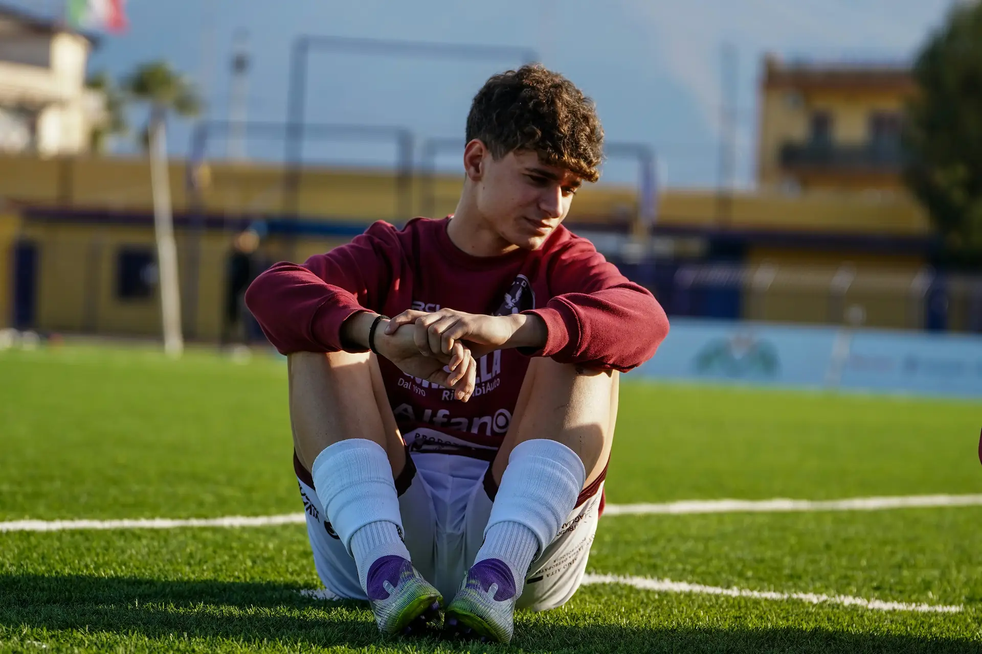 A young footballer sitting on the pitch, deep in thought