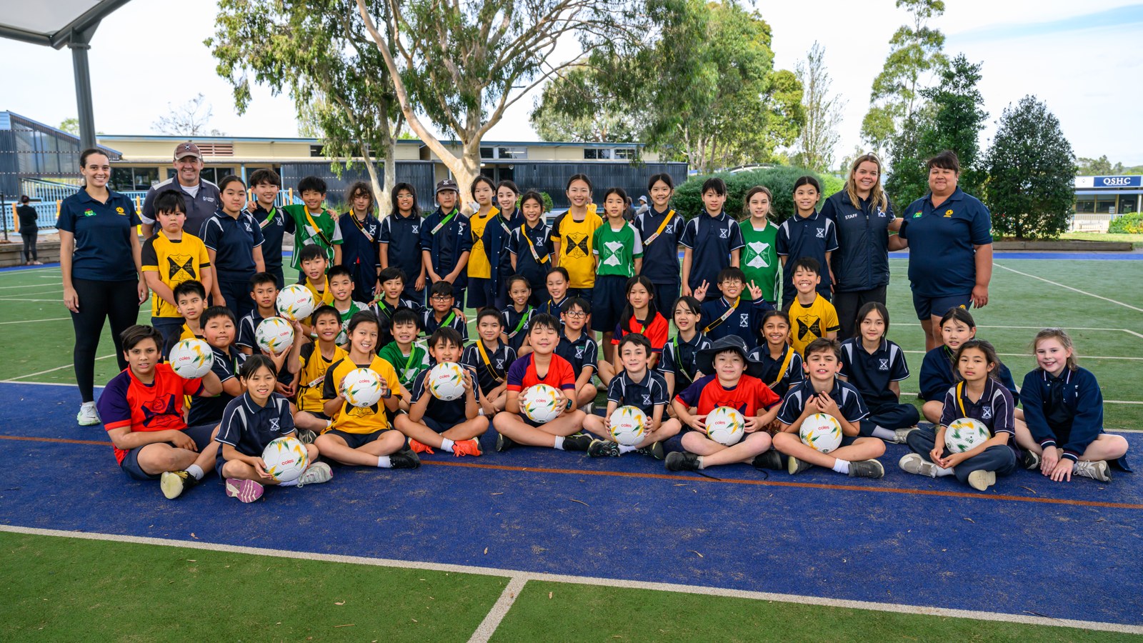 Australian school students in sports uniforms with footballs posing together on a school sports court during a sporting schools program