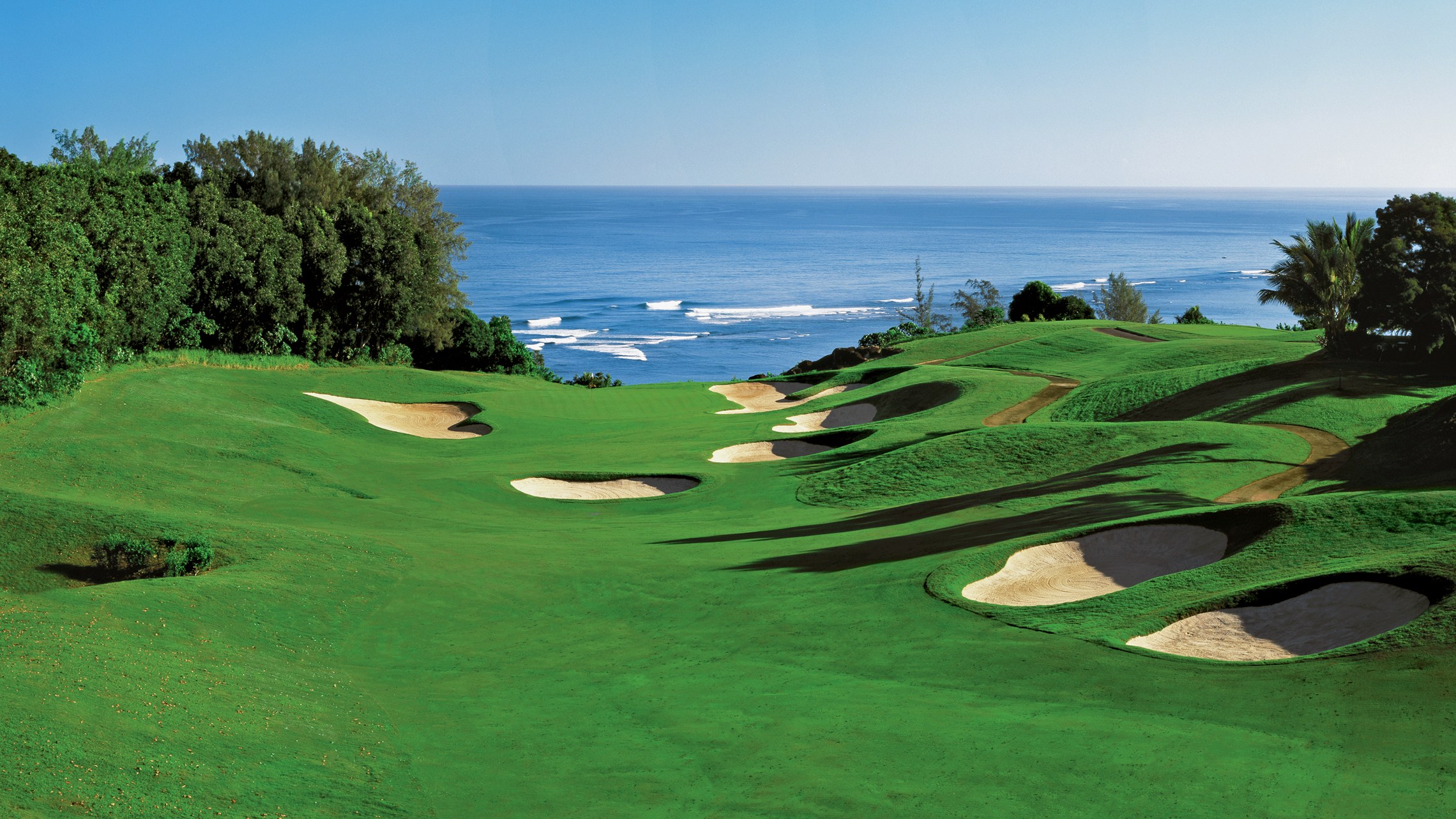 Lush green coastal championship golf course in Asia with bunkers, tropical trees and the ocean beyond