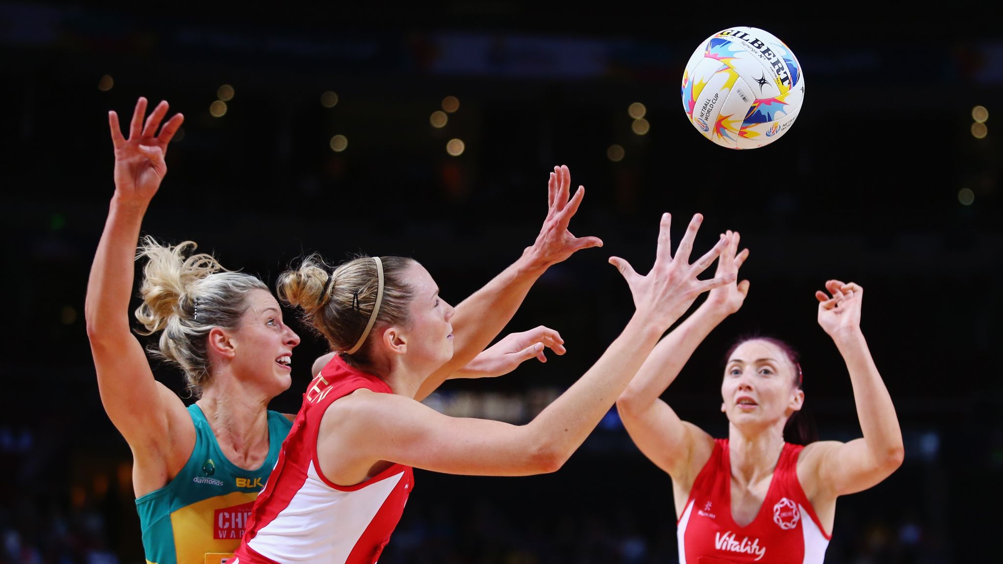 International netball players competing for the ball with a Gilbert match ball during a live netball fixture