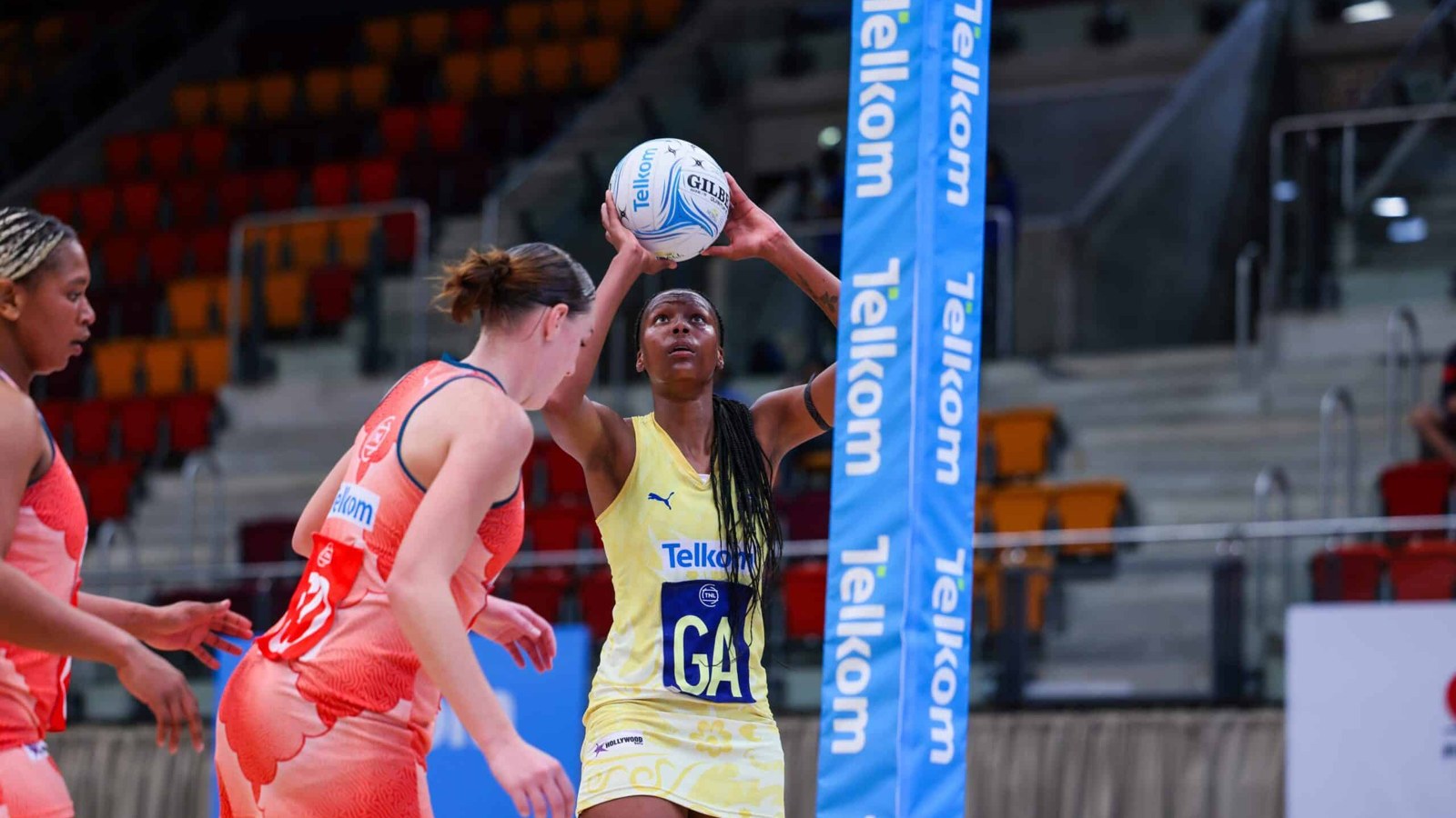 Netball players competing at a South African match, one player shooting for goal