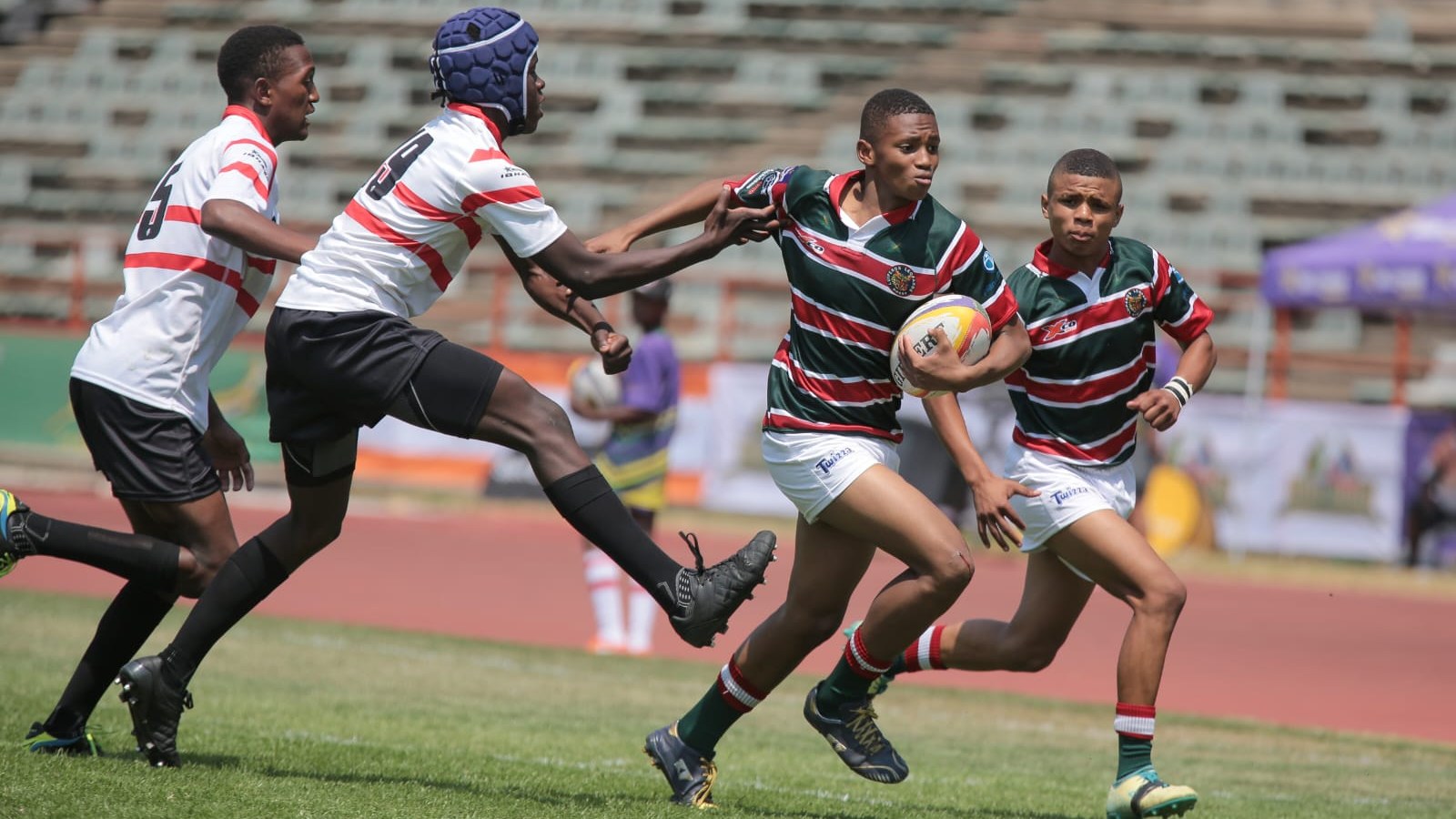 Young South African rugby players competing in a match, ball carrier breaking through a tackle