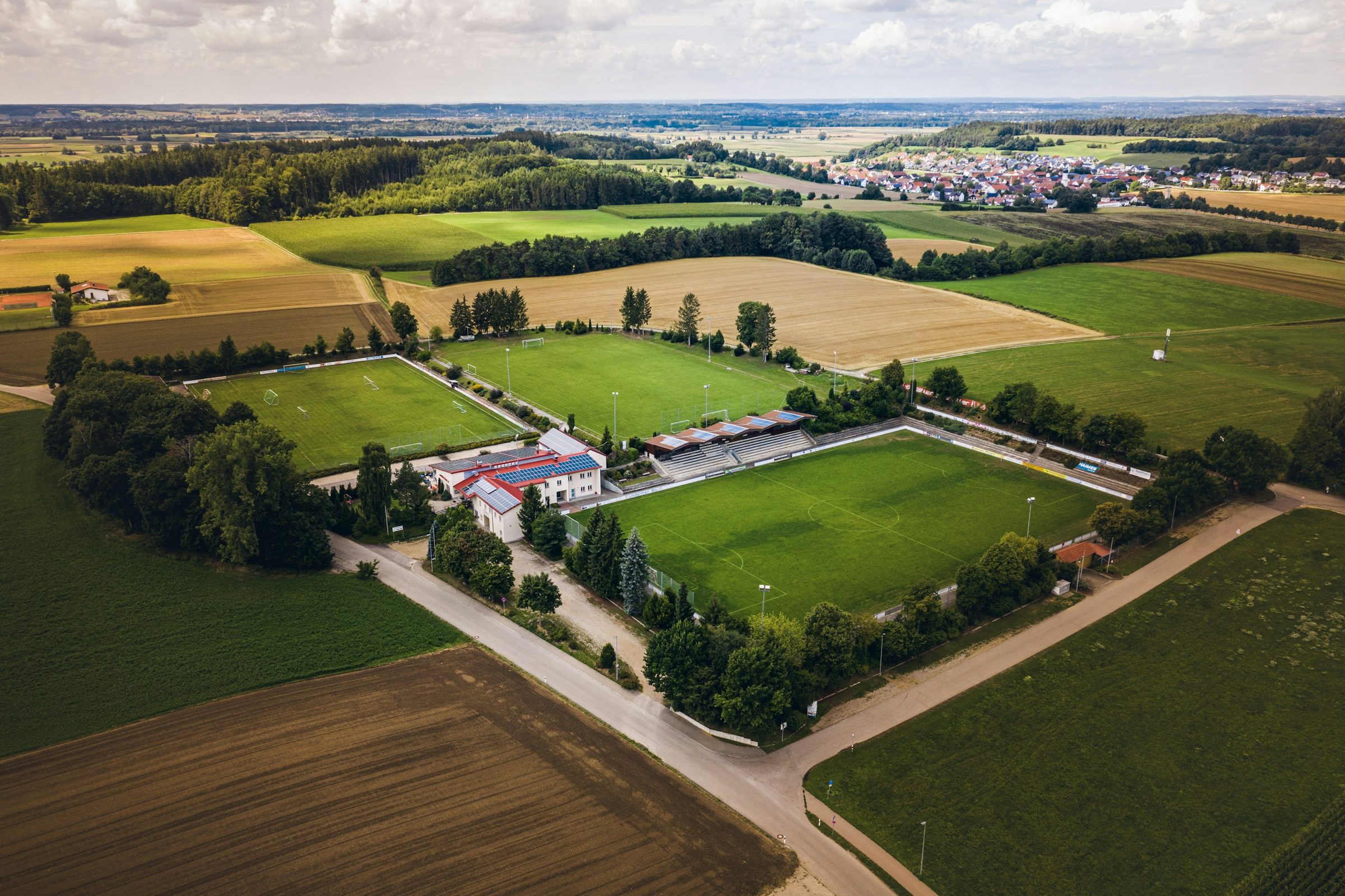 Aerial view of a football training complex with several grass pitches in the European countryside
