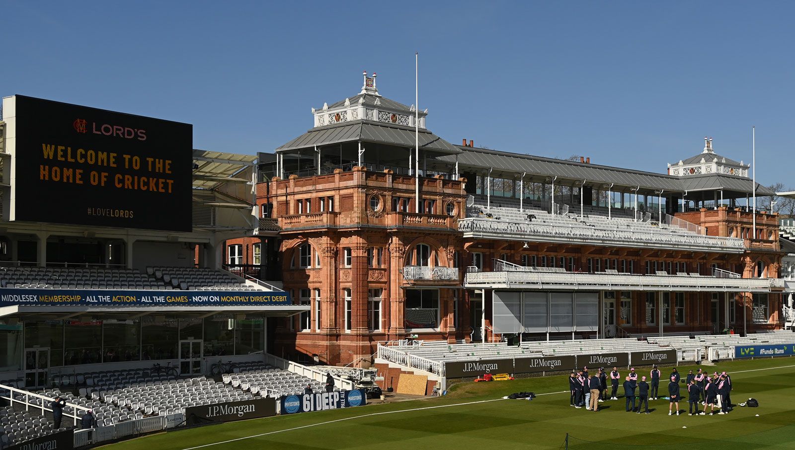 A cricket match being played on a green European cricket ground with a pavilion