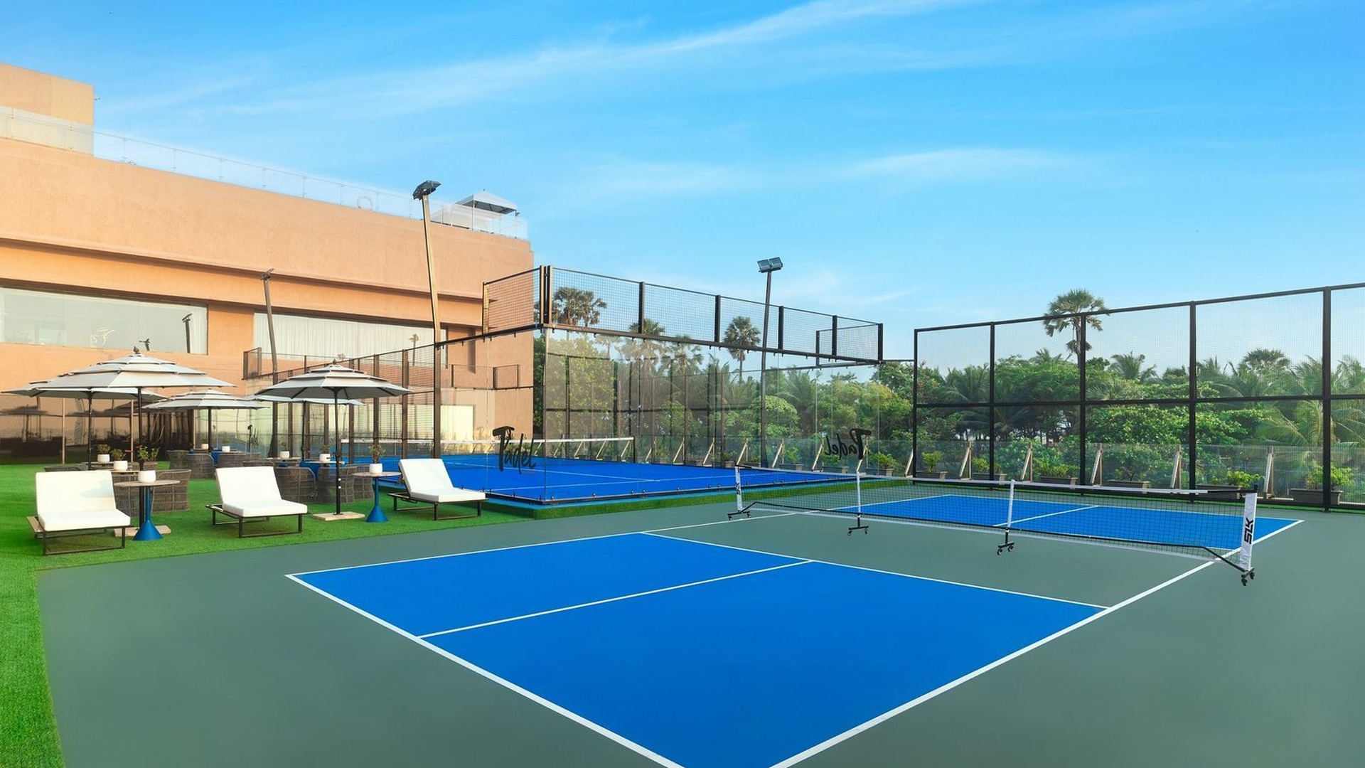 Modern luxury padel courts with blue playing surface, palm trees and resort loungers in an Asian setting