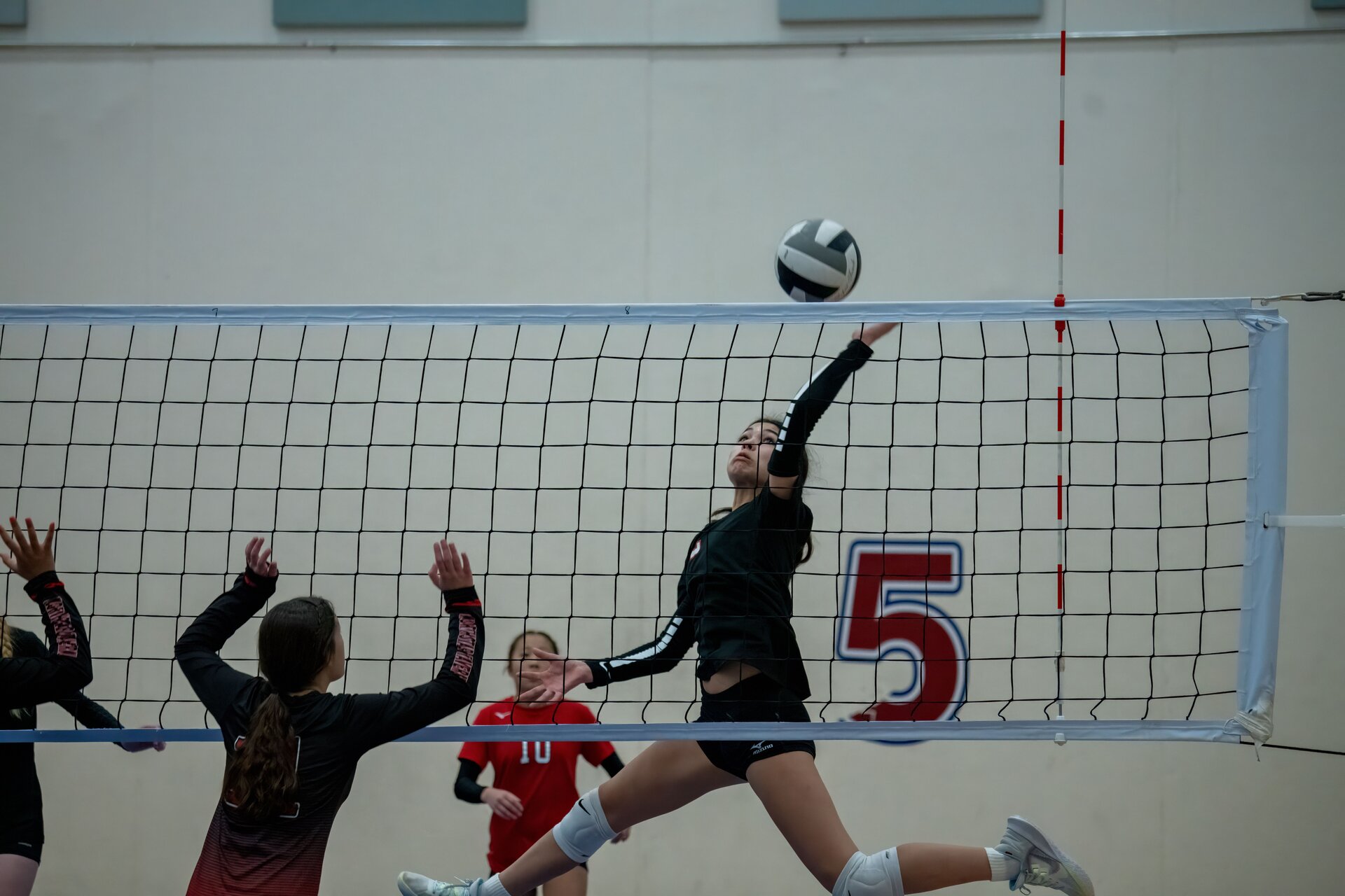 Teenage volleyball players competing on an indoor court